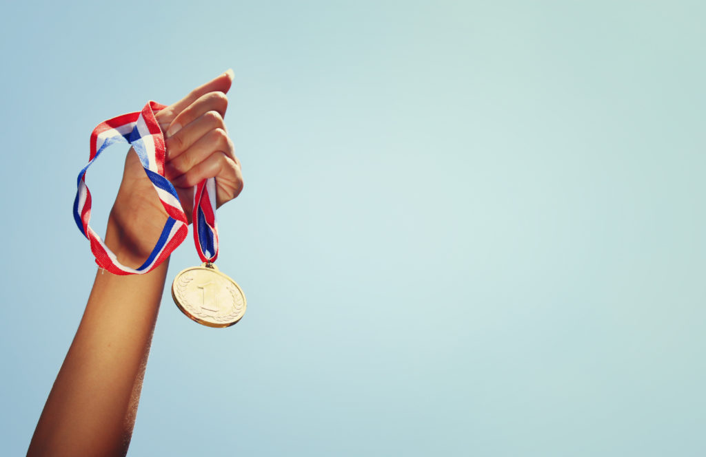 woman hand raised, holding gold medal against sky. award and victory concept